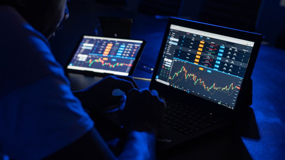 Trader reviewing financial charts and market data across multiple laptop screens